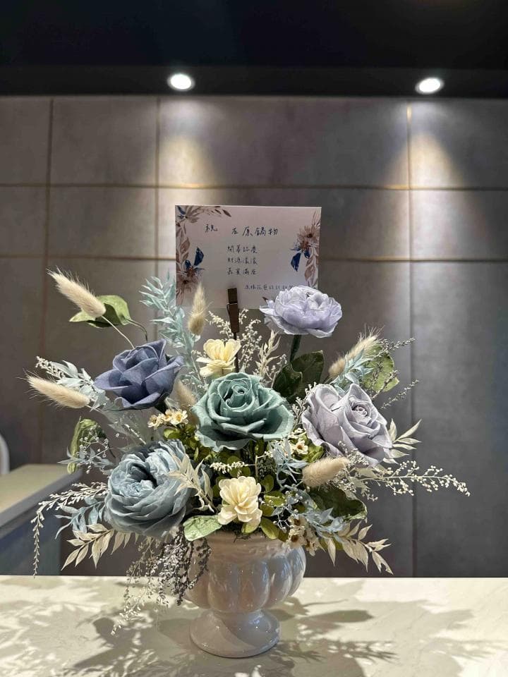 1) 照片顯示一個藍色和綠色的花束,放在一個白色的花瓶裡,花瓶有兩個手柄