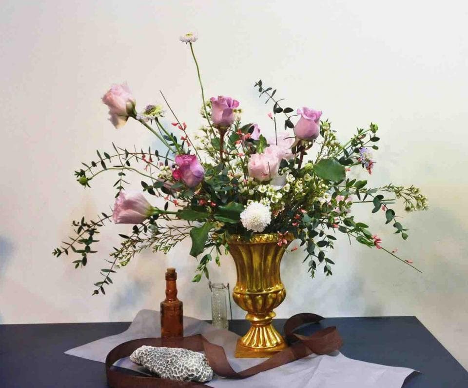 1) 照片顯示一個金色的花瓶,裡面擺滿了粉紅色的玫瑰花,旁邊還放了一個玻璃瓶