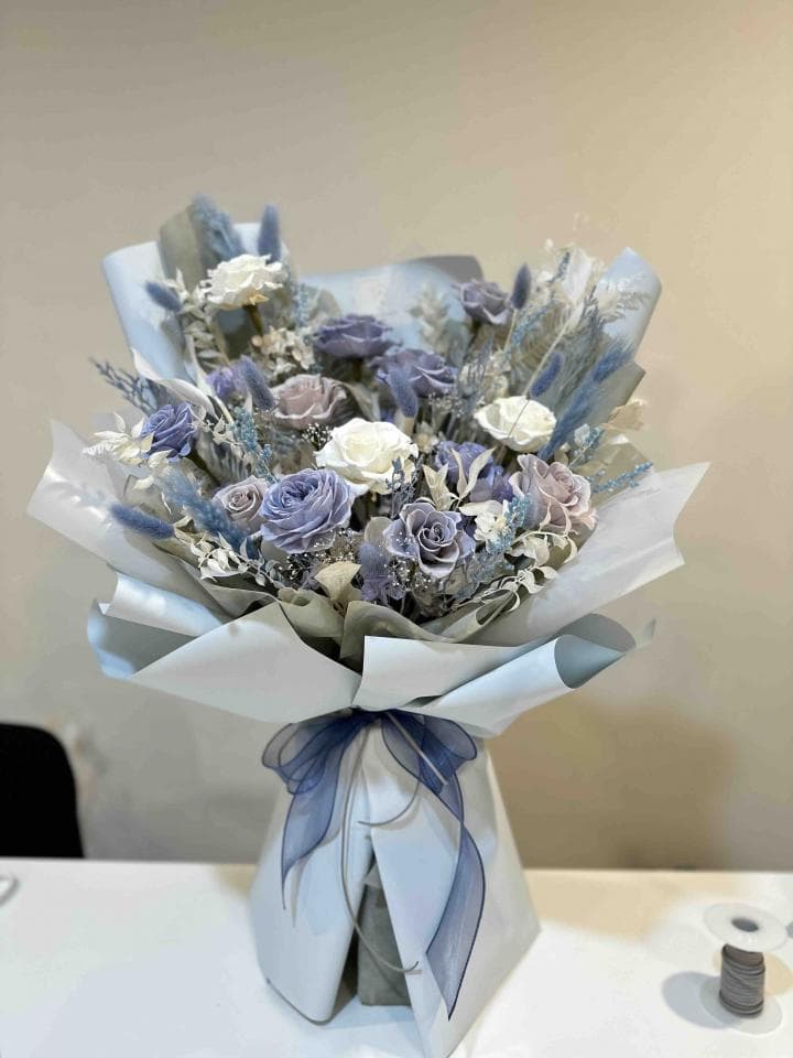 這張照片是一束用藍色和白色花朵組成的花束,被白色包裝紙包著,並用藍色緞帶綁起來。