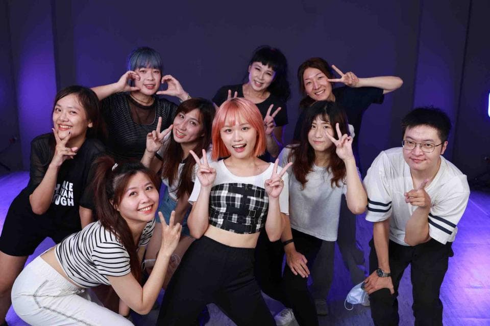 這張照片是一群年輕人擺出搞怪的姿勢,其中最搶眼的是穿著白色短袖上衣和黑色短褲的女生,她正對著鏡頭比出勝利手勢,笑容燦爛,展現出青春活潑的氣息。