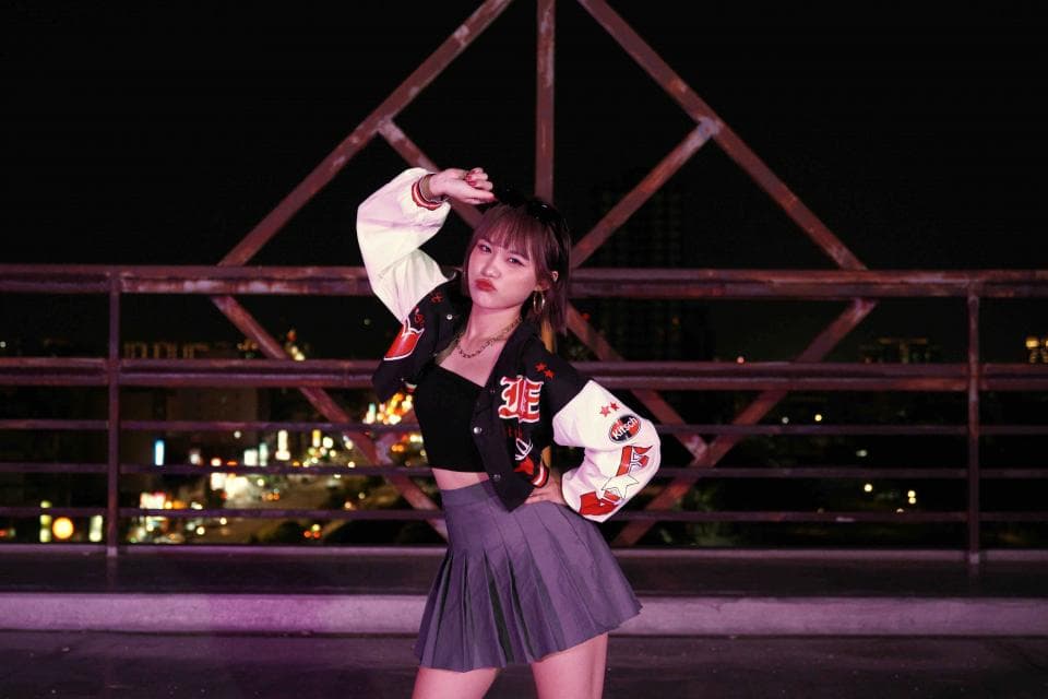 這張照片是一個身穿白色和紅色棒球外套的年輕女子。她的手放在頭上,她正看著鏡頭。