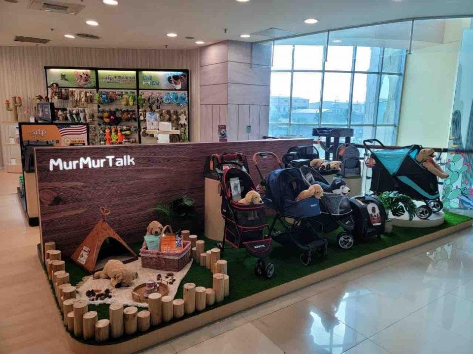 這張「寵物用品店」的照片是,展示了多款寵物推車和可愛的狗狗,旁邊還有木製裝飾和一個寵物帳篷。