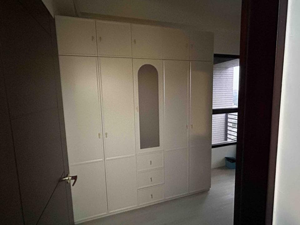 這張照片是一間臥室的一部分,照片中主要是展示了房間的衣櫃。衣櫃是白色的,設計簡潔,有鏡面和抽屜,整體風格清新明亮。