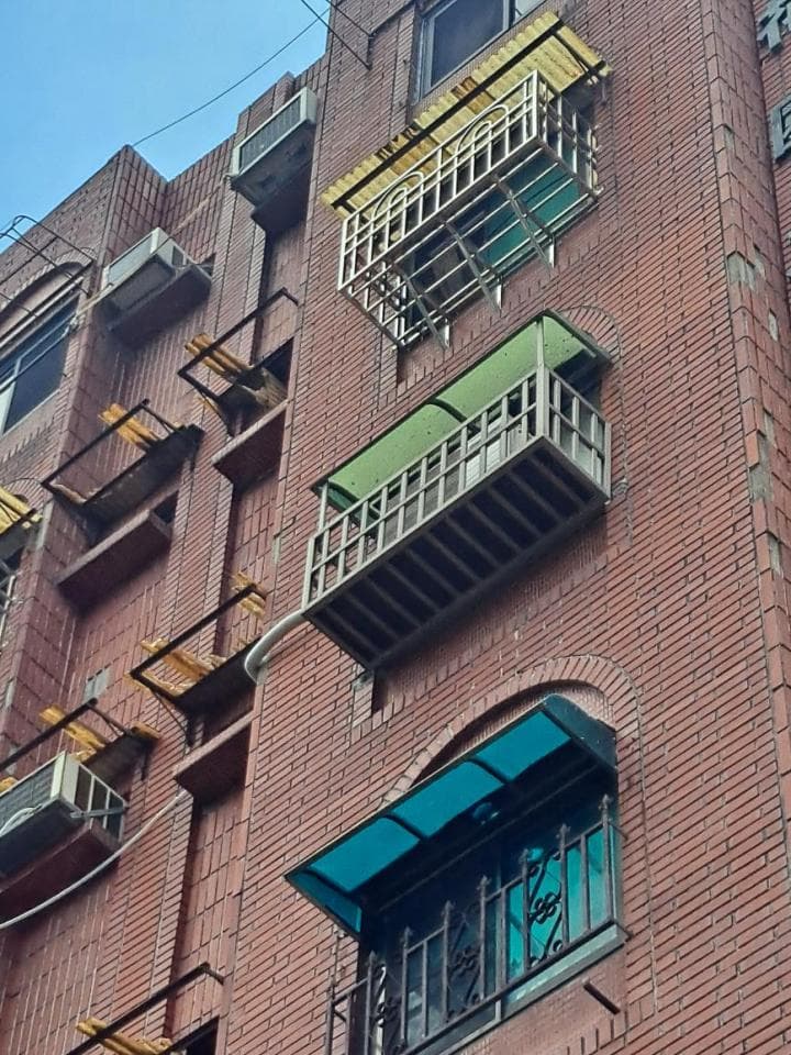 1) 這張照片顯示一棟紅磚建築的正面,建築物上有許多鐵製的窗戶和陽台,其中一個陽台有藍色的遮陽棚