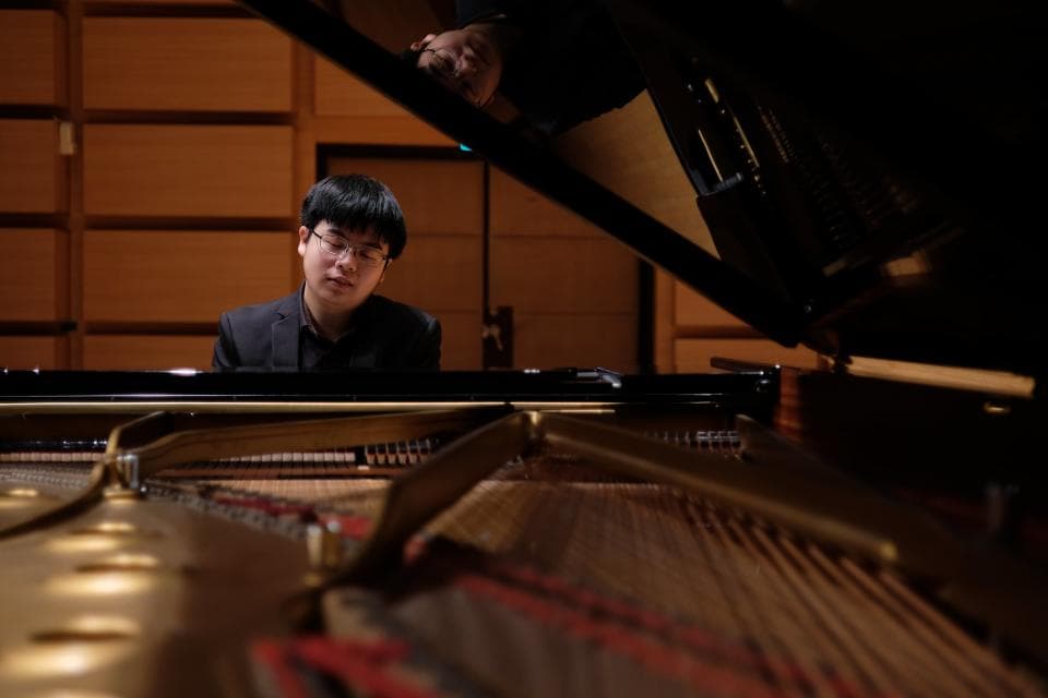 這張「鋼琴演奏」的照片是一位戴眼鏡的年輕男子坐在鋼琴前,準備演奏。