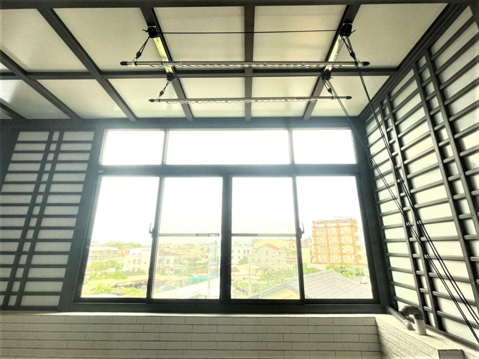 這張「室內」的照片是 一個有大型窗戶的房間,窗戶外可以看到城市景色。房間內有兩條黑色的晾衣繩,懸掛在窗戶上方。