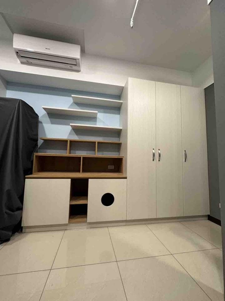 這張照片是一個房間的一角,最顯眼的是一面牆上安裝的白色櫃子,櫃子上有許多層板,可以放置物品。櫃子旁邊是兩扇白色門,門板上有黑色的把手。牆壁是淺藍色的,整體空間看起來很簡潔。