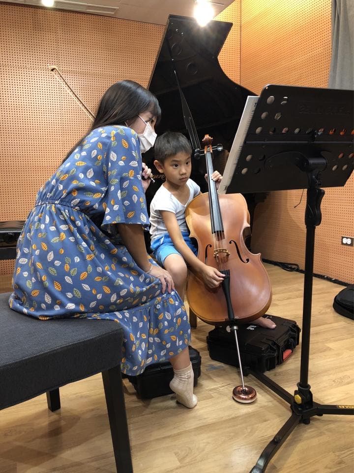 1. 照片中,一位身穿花卉圖案洋裝的女性站在一個男孩旁邊,男孩正拉著大提琴
