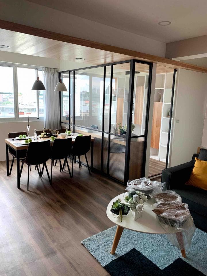 這張照片是一間現代化的公寓,最引人注目的地方是客廳和餐廳之間用黑色鐵框玻璃隔開的設計,讓空間看起來更寬敞明亮,也增添了時尚感。