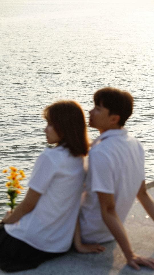 這張「一對情侶坐在海邊」的照片是一對年輕男女,他們穿著白色襯衫,面向大海,看起來很甜蜜。