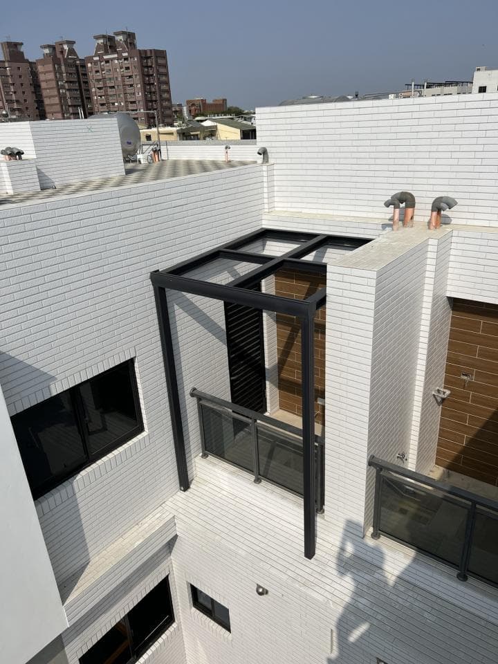 1) 照片顯示一個現代建築物,建築物採用白色磚牆,屋頂上有一個黑色的鐵製陽台,陽台周圍有玻璃圍欄