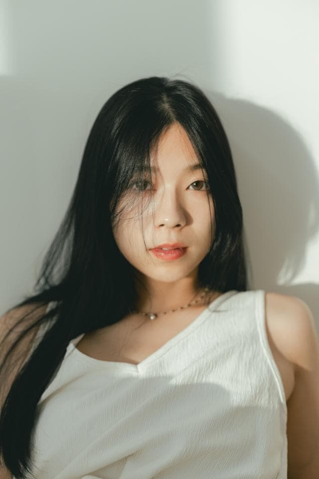 這張照片是一個年輕女性的照片,她有著一頭烏黑的長髮和一雙明亮的眼睛。她穿著一件白色的背心,看起來很優雅。