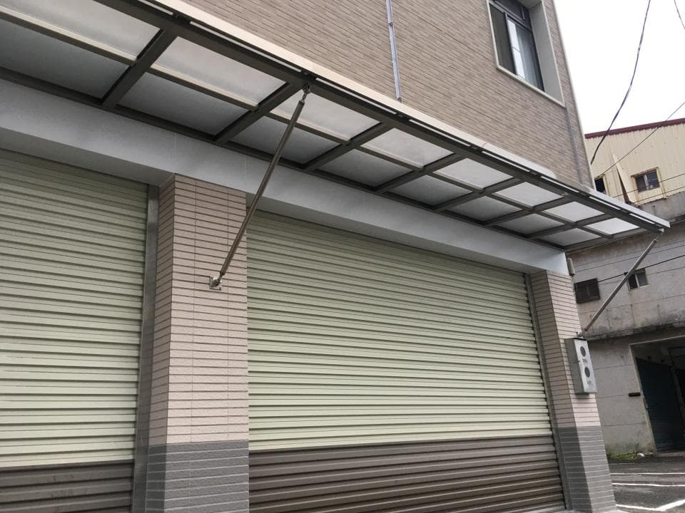 1. 照片顯示一間建築物的側面,建築物外牆為淺棕色,有一扇捲門,捲門上裝設遮雨棚