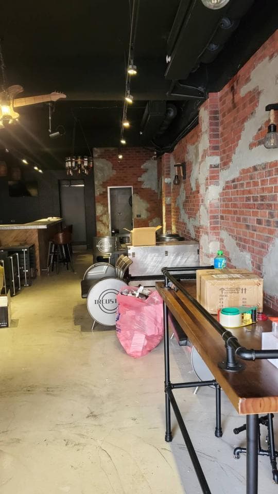 這張照片是一個酒吧的內部,最重要的部分是吧檯,它由木頭和黑色鐵管製成,上面擺放了一些酒瓶和杯子。