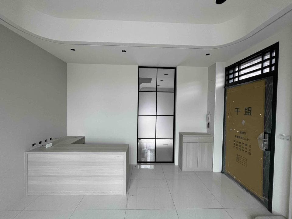 這張照片是室內的一角,最顯眼的是一個木紋的L型櫃台,櫃台表面光滑,木紋清晰。櫃台設計簡潔,與背景牆面形成對比,更突顯其存在感。