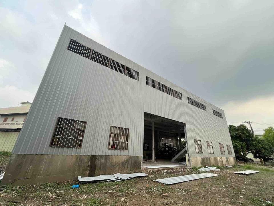 這是一張拍攝於白天、灰白色、金屬外牆的建築物照片,建築物旁有草地