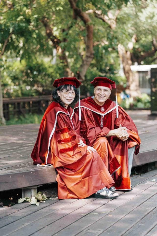 這張照片是一對夫婦,他們都穿著紅色的畢業袍,坐在木板上的階梯上,看起來很開心。