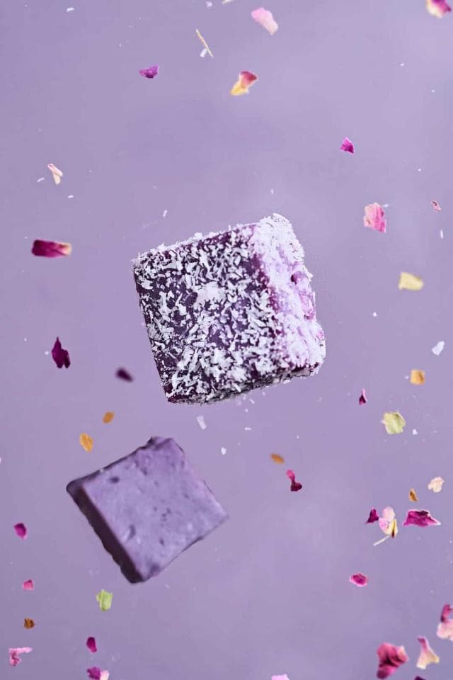這張照片是兩塊方形的紫色甜點,上面覆蓋著白色椰蓉,在淡紫色的背景上漂浮著。
