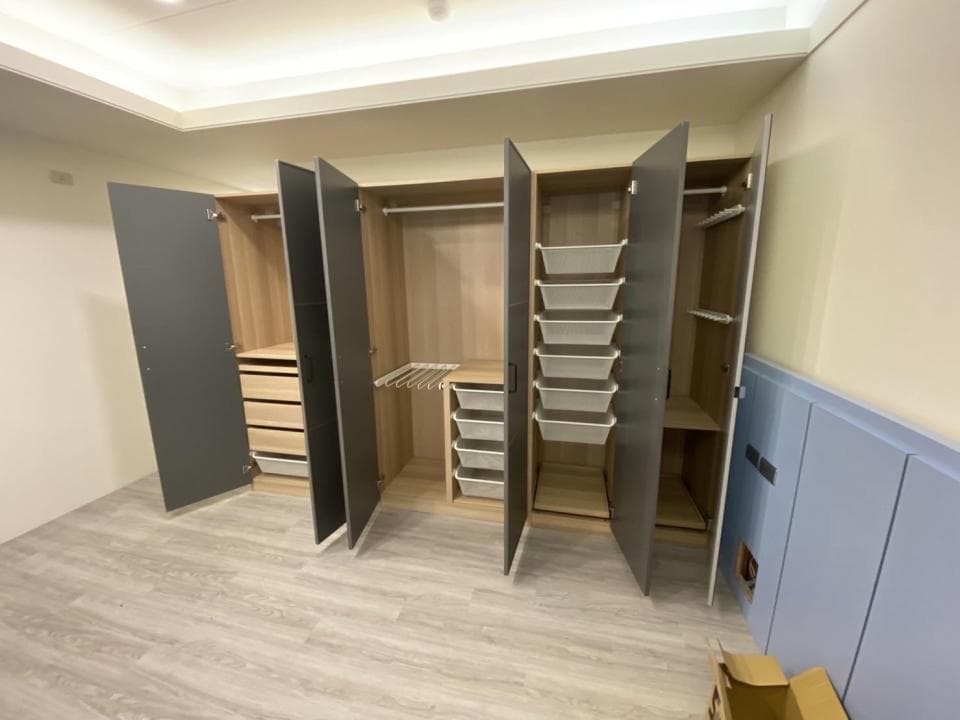 這張照片是一間現代化的臥室,最主要的部分是衣櫃,它由六個門板組成,其中三個是深色的,另外三個是木色的。衣櫃內有許多層架和抽屜,可以放置衣服、鞋子、包包等物品。