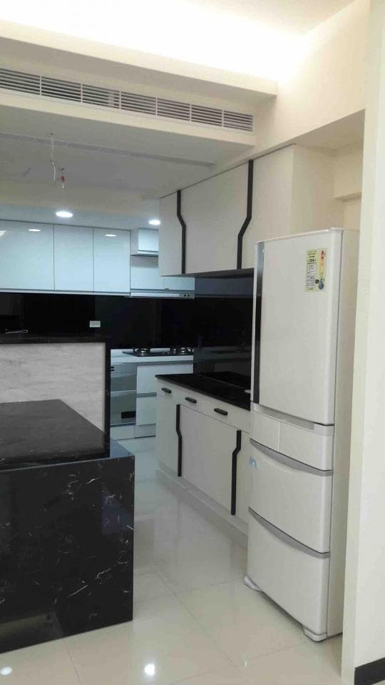 這張照片是一間廚房,最重要的部分是冰箱,它位於右邊,是一個白色雙門冰箱,上面有兩個抽屜。冰箱旁邊是白色櫥櫃,整體簡潔明亮。