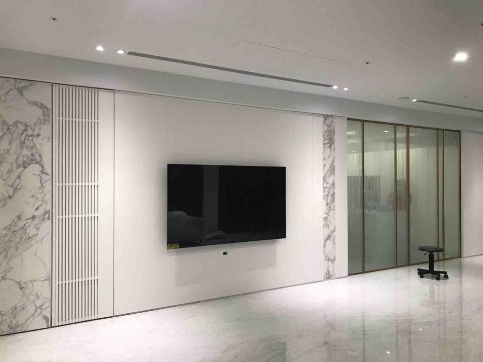 1) 照片顯示一個現代風格的客廳,牆壁上裝飾著白色大理石紋路的牆板,中間有一台大型電視,右邊是一個透明的玻璃門,玻璃門後面的空間可見模糊的物品