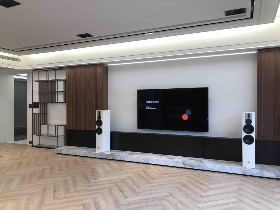 這張照片是一間現代化的客廳,最重要的部分是電視牆,電視牆上有一台大型液晶電視和兩台高音質音響,電視牆下方的石材台面顯得非常高級。