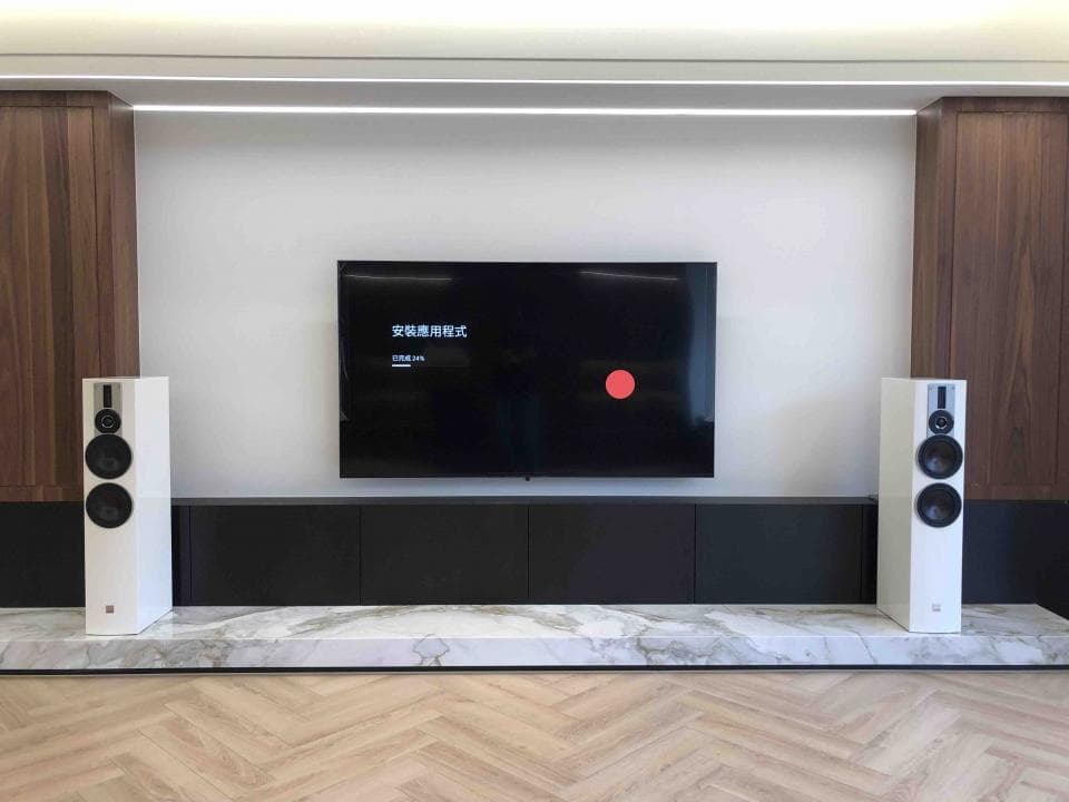 這張照片是一個現代化的家庭影院,最重要的部分是電視機和音響系統。電視機尺寸很大,螢幕顯示著黑色畫面,而音響系統則是由兩台白色音箱組成,擺放在電視機下方。