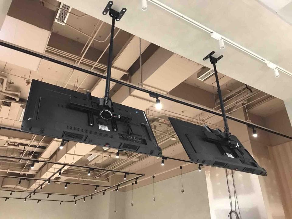 這張照片是兩台電視安裝在一個現代化的天花板上的。電視機是從天花板上吊下來的,並使用支架固定,這種安裝方法可以最大限度地利用空間,並使電視機看起來更美觀。