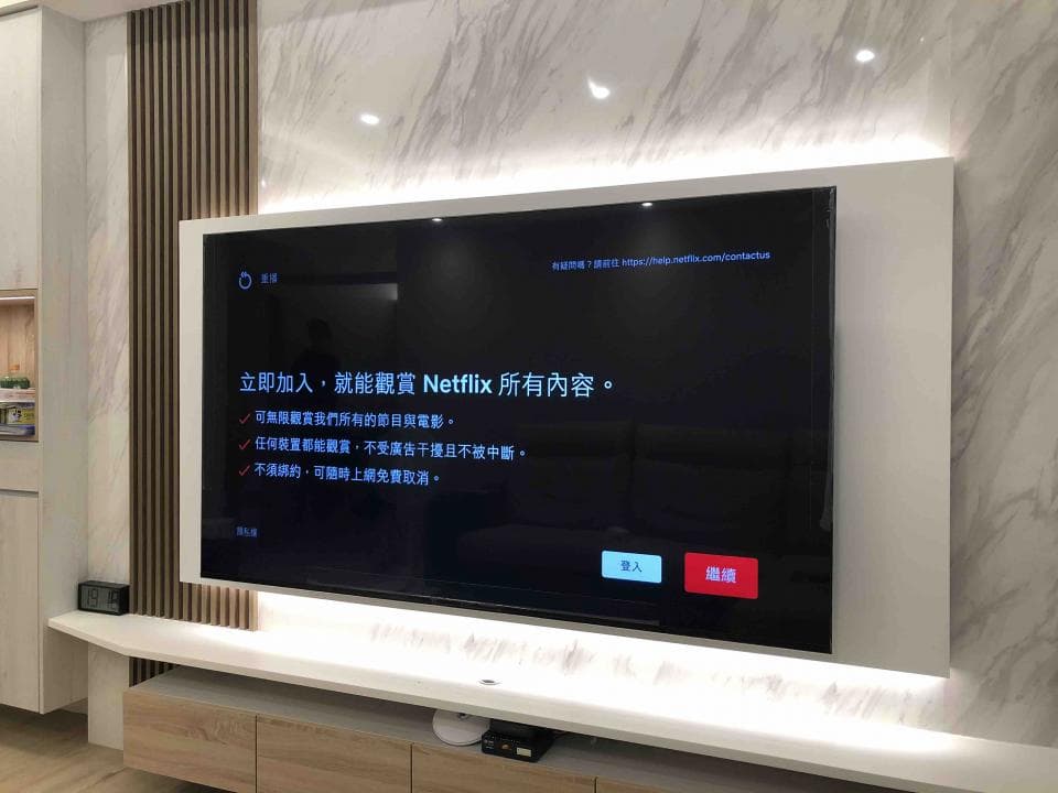 1) 照片顯示電視上正在播放 Netflix 的歡迎畫面,電視下方是電視櫃,櫃子上方有燈帶