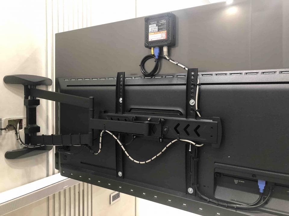 1) 照片顯示一個黑色的電視安裝在牆上,電視上有幾條線,其中一條線連接到一個黑色的盒子