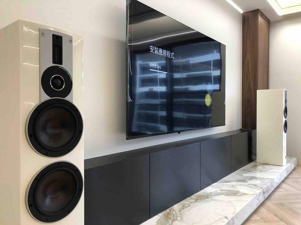 1) 照片顯示一個現代客廳,其中有兩個白色揚聲器,一個大型電視和一個黑色大理石櫃