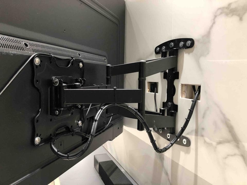 這張照片是一台電視安裝在牆上,電視背後有黑色的支架,支架上有很多線。