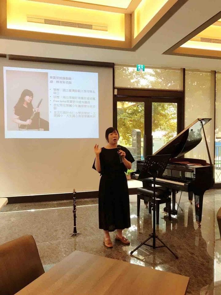 這張照片是一位女士站在舞臺上,正在用麥克風唱歌,她穿著黑色的連衣裙,看起來很優雅,舞臺上放著一把黑色的鋼琴,背景是一面巨大的屏幕,上面顯示著一些文字,畫面看起來很溫馨。