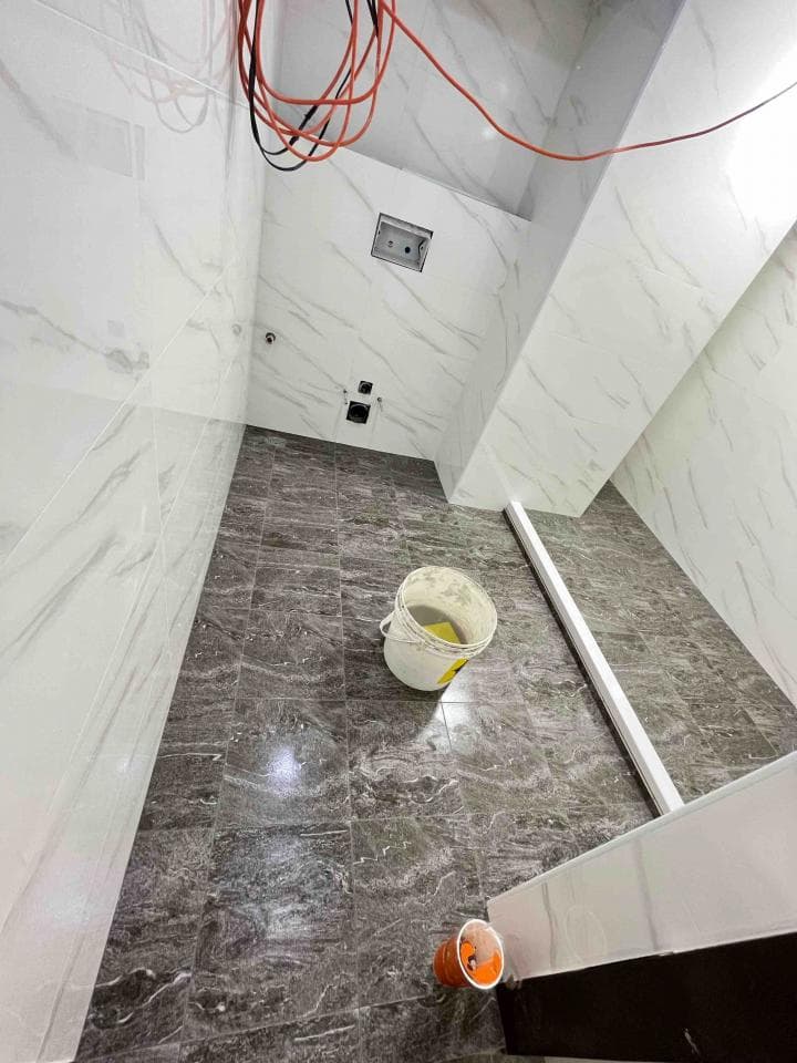 1) 照片顯示一個正在裝修的浴室,天花板上有紅色電線,牆壁是白色的,地板是灰色的