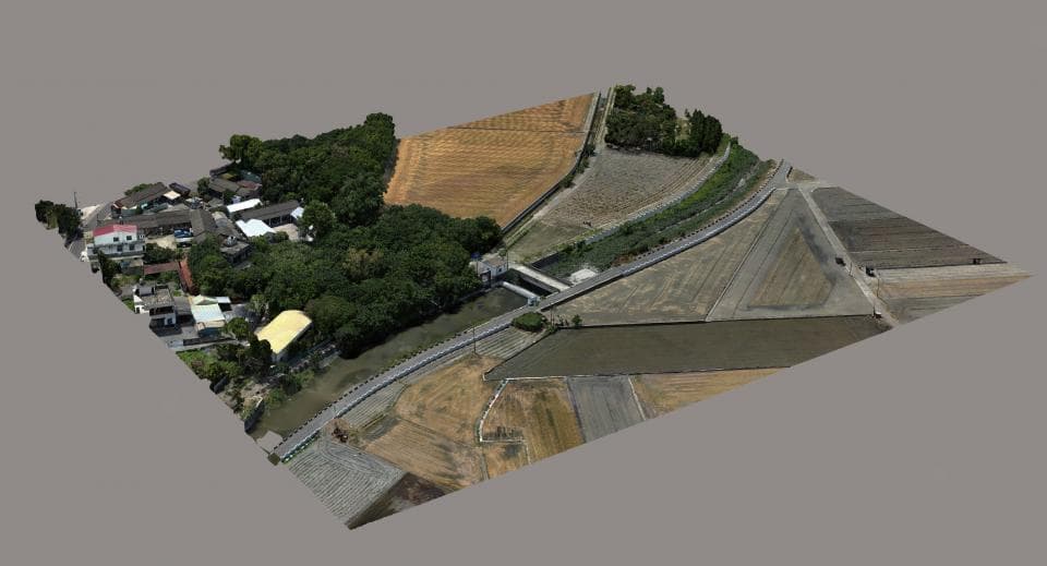 這張「俯瞰圖」的照片是一片綠色的田野,中間有一條蜿蜒的河流,河流上有一座橋樑,橋樑旁邊有一片房屋。