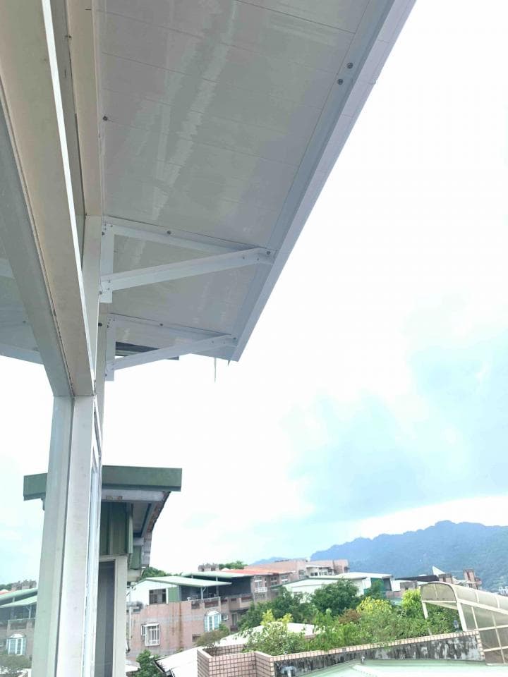 1) 照片顯示一個白色的遮雨棚,遮雨棚安裝在建築物的牆壁上,遮雨棚的下方可以看到一些建築物和山脈