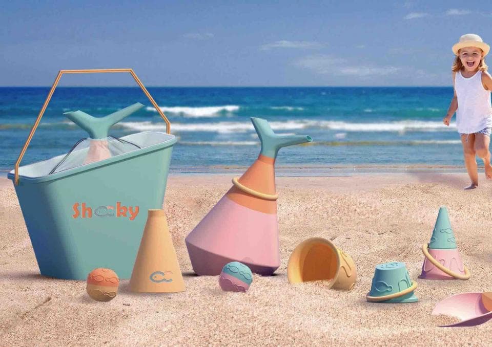 這張照片是一個海灘上玩耍的場景,最重要的是一個印有「Shoky」字樣的藍綠色桶子。桶子造型可愛,很適合小朋友玩沙。