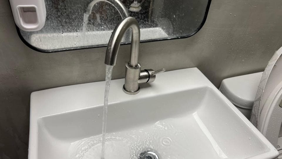 1) 照片顯示一個浴室洗手台,上面有一個水槽,水龍頭正在出水,水流入水槽