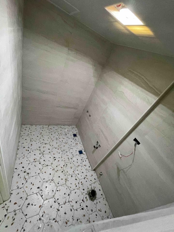 1) 這是一張浴室的照片,照片中顯示的是浴室的牆壁和地板,牆壁上裝修了白色瓷磚,地板上鋪設了白色六角形瓷磚,其中間還點綴著一些黑色的碎石