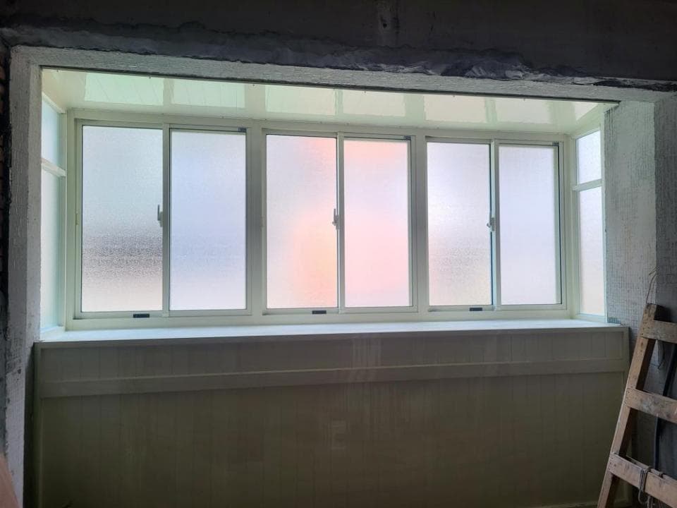 1) 照片顯示一個房間內的一扇大窗戶,窗戶為白色窗框,由三塊玻璃組成,窗戶上半部為霧面玻璃,下半部為透明玻璃,窗戶下方為白色木板,房間牆壁為淺色,窗戶右側牆壁角落有一架木梯