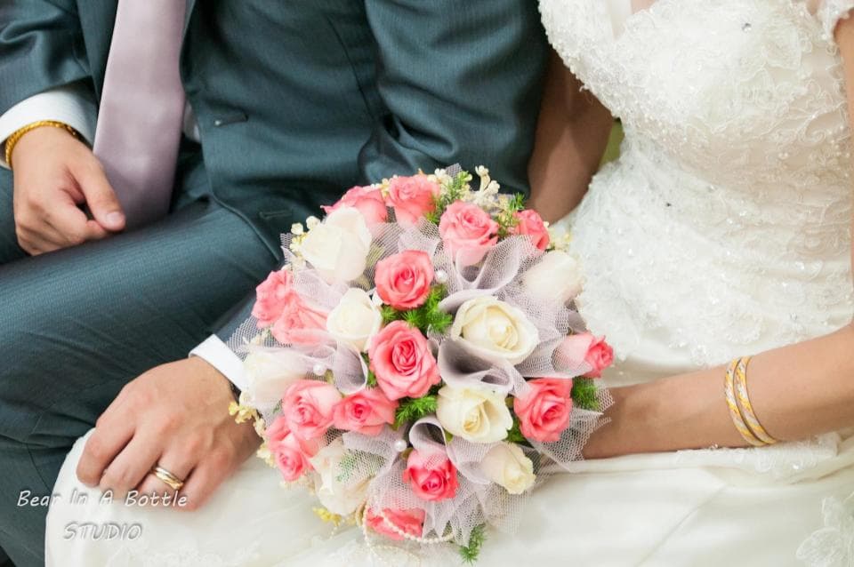 這張照片是一對新人手持婚禮花束,花束裡有粉紅色和白色玫瑰,以及一些綠葉。