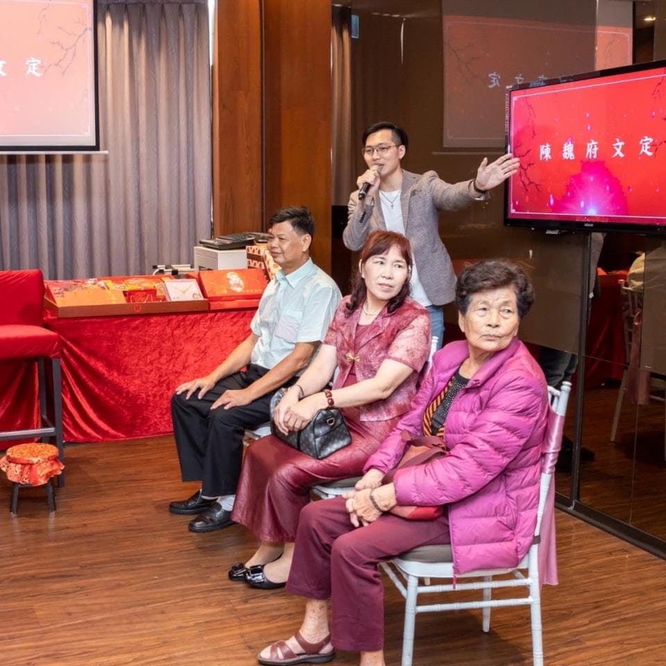 這張「婚禮」的照片是,一對新人正在台上接受親朋好友的祝福,台下坐著他們的親朋好友,其中一位男性朋友手持麥克風,正在說話。