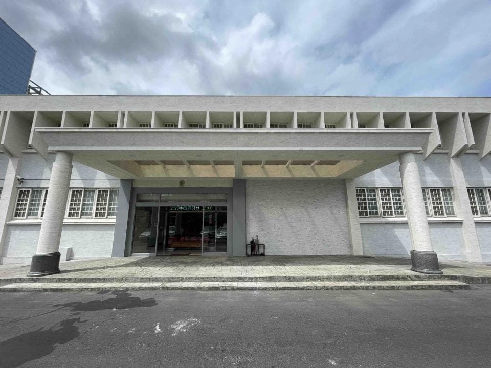 這張照片是一個現代化的建築物,最重要的是建築物前面的入口,有兩根柱子撐著一個遮陽棚,棚下是玻璃門,門前有兩層台階,台階上還放了幾個黑色垃圾桶。