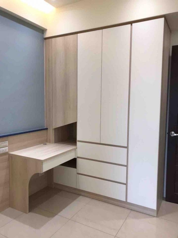 這張照片是一個房間的角落,最重要的是一個白色的衣櫃和一個木頭的書桌。衣櫃有四個抽屜,書桌的桌面可以摺疊起來,是一個很實用的設計。