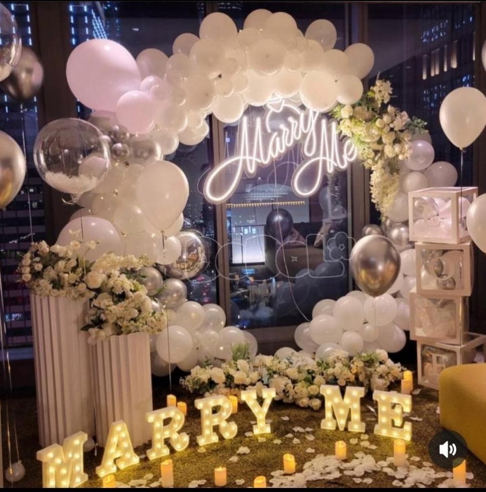 這張照片是一個求婚場景,最重要的是用氣球和燈光裝飾的「Marry Me」字樣。