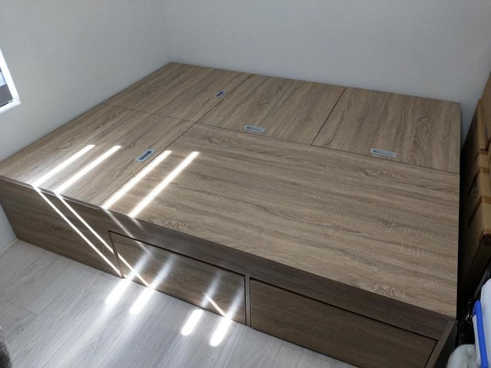 這張照片是一張帶有儲物空間的床,床板可以打開,露出底部的收納空間。床的材質看起來像是木頭,顏色是淺棕色,整體給人一種簡潔大方的感覺。