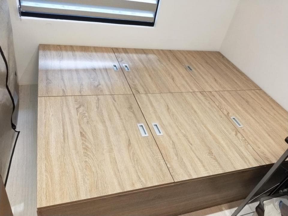 這張照片是一個木質床架,它有四個抽屜,每個抽屜上都有一个銀色的把手。床架的木紋清晰可見,呈現出自然的質感。