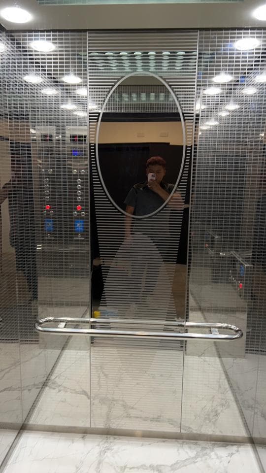 1) 電梯內部,鏡面牆上有一個橢圓形鏡子,鏡子反射了一個人的影像,地板上鋪著白色大理石