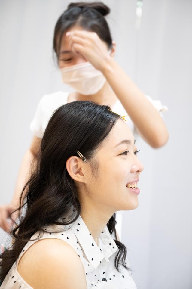 這張照片是一名女子正在幫另一名女子整理頭髮,她們正在準備出席重要場合。被整理頭髮的女子正在微笑,看起來很開心。