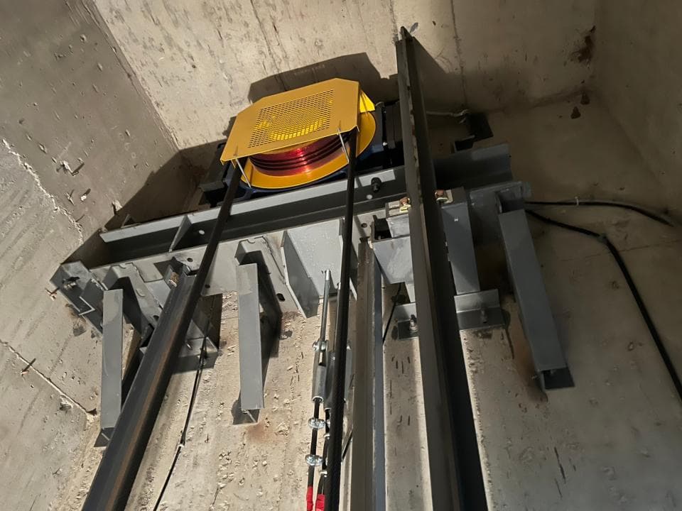 1) 這張照片顯示電梯機房內部,其中一個電梯的配重繩輪組裝在混凝土牆壁上